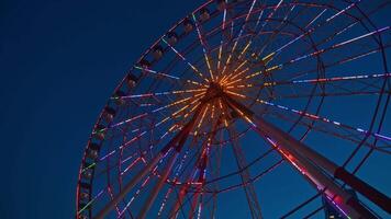 View from below of a large and impressive Ferris wheel, sparkling with colorful lights and full of tourists and passengers, against the backdrop of a clear night sky. video