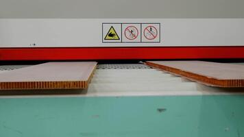 Plastic panels used in construction industry and furniture manufacturing are fed into gluing machine, which displays warning labels indicating potential hazards to factory workers. video