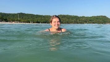 Smiling Caucasian woman swimming in the ocean with lush green coastline, perfect for summer vacations or beach holidays video