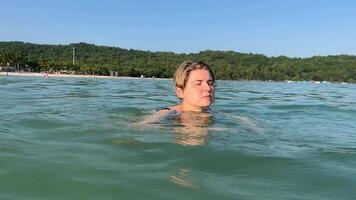 A Caucasian woman swims peacefully in clear tropical waters with a lush coastline in the background concepts, relaxation, vacation, summer holidays video