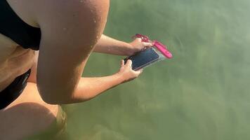 A woman places a phone in a waterproof case while standing in clear water, perfect for summer vacations and beach safety video