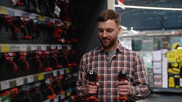 A man in a hardware store chooses a new screwdriver next to a showcase of power tools for repairs in the house video