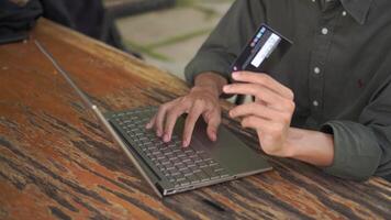 High angle view of man hand working on his laptop while holding a credit card. Man trying to online purchasing with card video