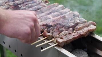 young man grilling meat kebabs on coals, ARROSTICINI - typical southern Italian cuisine, a luxurious picnic on the terrace near the house in summer,aromatic smoke rises from the barbecue, video