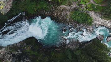 Aerial view of a waterfall merging into a turquoise river in a lush green forest video
