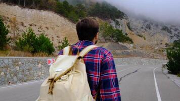 a man with a backpack walks alone on a mountain road. One 30s Tourist Walks on an Adventure Trip in Natural Landscape in Hike on a Environment video