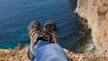 Close up POV of hiking boots of an independent male traveler on top of a mountain, looking at the view on ocean and cliff. video