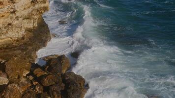 Sea waves breaking against cliff and make a rainbow, a beautiful sunset light. viewed from above. video