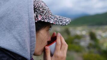 Traveler asian girl picnic at nature in cloudy day. camera focused on face and cup in hands, traveler young woman enjoying drink and scenic view of mountain video