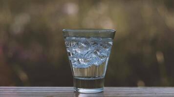 Mineral water in a glass with ice cubes stands on the nature. Relaxing in Vacations on Summer. video