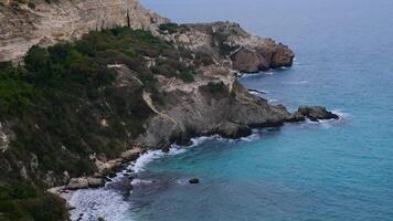 The view from the bird's eye view on the steep coast with crystal clear turquoise sea, waves breaking on the rocks and cliffs. Blue ocean waves. video
