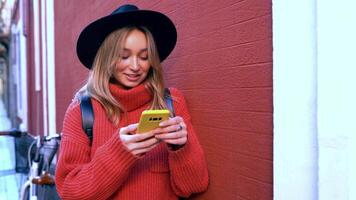 Blonde woman typing and reading text messages on her smartphone in front of a red wall. video