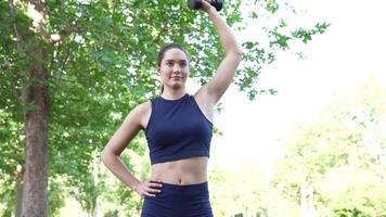 ajuste mujer ejercicios en un parque con mancuernas, demostración atletismo y determinación en su rutina video