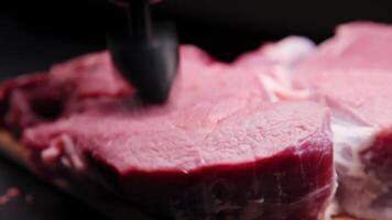 Close-up of a hand with a portable massager on a black background, a piece of meat being beaten by the massager video