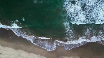 a artístico aéreo Visão mostra ampla ondas falhando contra uma arenoso praia, criando interessante padrões em sawarna praia, banten, Indonésia. video