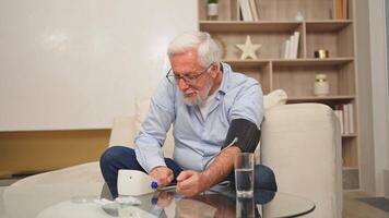 Hypertension problem in senior age. Old man measuring blood pressure with tonometer at home. Senior man have health problem making self checkup. Headache treatment of hypertension hypotension video