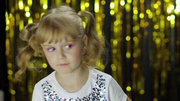 Stylish child dancing fooling around, make faces. Girl posing on background with foil golden curtain video
