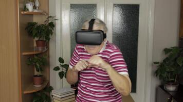 Grandmother in virtual headset glasses watching in VR helmet training box, shows fist fight video