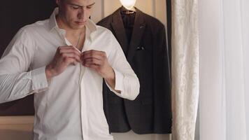 Stylish man in jacket fastens buttons, buttoning white shirt preparing to go out near window video