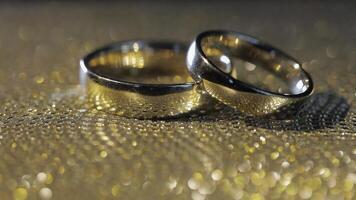 Wedding rings lying, rotate, spinning on shiny golden shining surface with light, close-up macro video