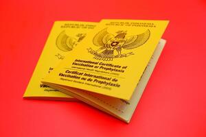 international certificate of vaccination or prophylaxis isolated on red background. yellow book as a sign of vaccination. 2 yellow books of vaccines from Indonesia photo