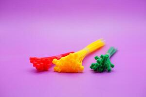 bundle of zip ties isolated on purple background. zip ties in red, green, and yellow colors arranged in a row. Cable ties or cable ties, straps that can be used for various purposes. photo