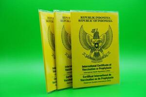 international certificate of vaccination or prophylaxis isolated on green background. 3 yellow books as a sign of vaccination. yellow book of vaccines from indonesia photo