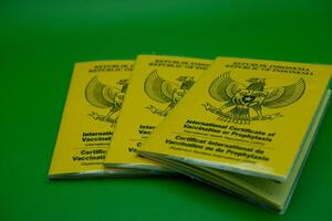 international certificate of vaccination or prophylaxis isolated on green background. 3 yellow books as a sign of vaccination. yellow book of vaccines from indonesia photo