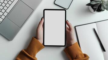 Female hands holding tablet with blank screen mockup at minimalist workspace. Laptop, notepad, plant. Work productivity. Digital technology template advertising image. Mock up realistic photo