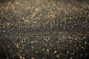 Golden glitter spreads across a dark surface, sparkling in the soft light photo