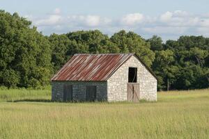 Abandoned stone barn in a field surrounded by trees during a sunny day photo
