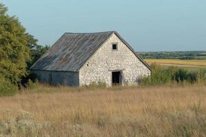 Old stone barn surrounded by tall grass on a clear day in the countryside photo