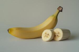 A ripe banana beside two freshly cut banana pieces on a light background photo