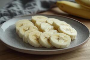 Sliced banana arranged neatly on a plate with whole bananas in the background on a kitchen table photo