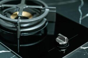 close up a single gas burner on a modern kitchen cooktop. The burner features a sleek black cast iron pan support. The surrounding cooktop surface is a glossy black. photo