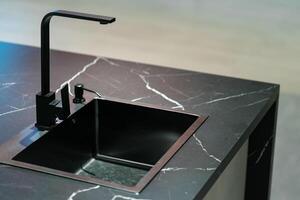 a sleek and modern kitchen sink and faucet set against a backdrop of dark cabinetry and a marble countertop. The faucet is a single-handle design with a tall, arched spout and a black matte finish. photo