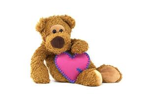 Cute teddy bear holding a pink heart with delicate blue stitching isolated on white background photo