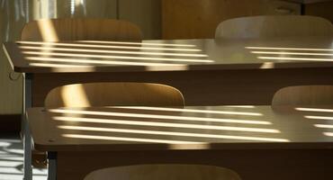 Empty classroom with wooden desks and sunlight casting shadow lines photo
