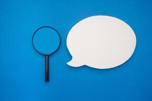 Top view of a blank speech bubble and a magnifying glass on a blue background photo