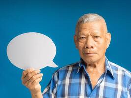 Senior man holding a blank speech bubble and looking at the camera with a smile while standing on a blue background photo