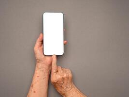 Top view of old woman hand holding a mobile phone with copy space for text over a gray background photo