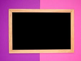 Top view of empty blackboard with a wooden frame over a purple and pink background photo