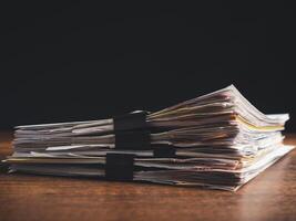 Stack of documents with binder clips on a wooden table with a black background photo