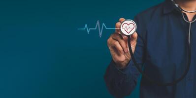 Hand of a doctor holding a stethoscope with a red heart icon while standing on a blue background photo