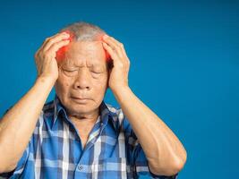 Senior man suffering headache pain while standing against a blue background photo