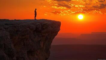 Silhouette of a man standing on a cliff edge at sunset. Concept of adventure, success, freedom and challenge. photo