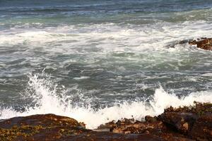 Wave Splashing Against Rocky Coastline With Rough Waters Under Cloudy Sky photo