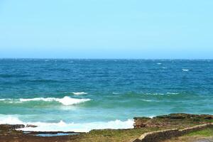 Bright Blue Ocean Waves Crashing Against The Rocky Shoreline On A Clear Day photo