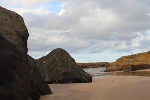 Close-Up View Of Rocky Beach With Sand And Large Boulders Under Cloudy Sky photo