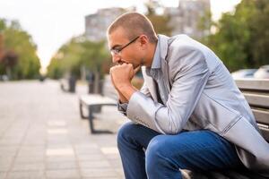 Portrait of thoughtful and worried man. He is sitting on bench in the city and thinking. photo